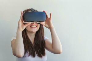 Smile young woman wearing using virtual reality VR glasses helmet headset on white background. Smartphone using with virtual reality goggles. Technology, simulation, hi-tech, videogame concept. photo