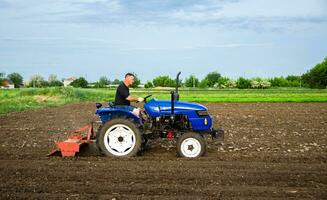 A farmer on a tractor cultivates a field. Farm work. Milling soil, Softening the soil before planting new crops. Plowing. Loosening surface, land cultivation. Farming, agriculture. photo