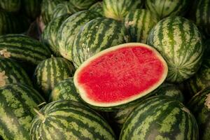 Red ripe sweet green watermelon cut in half on a pile of ripe watermelons. A red cut large watermelon in market. photo