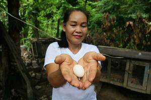 retrato de un contento asiático mujer participación un orgánico pollo huevos a el rural granja. foto
