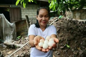 asiático mujer participación huevos en su manos en el granja con contento rostro. foto