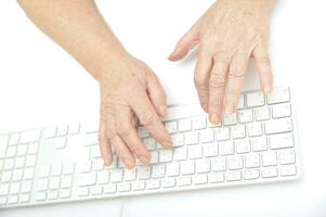 Hands of an old female typing on the keyboard, isolated on white, close-up. photo