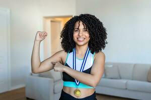 Attractive young African female athlete posing with her gold medal flexing her muscles proudly. African American Athlete showing first place medal photo