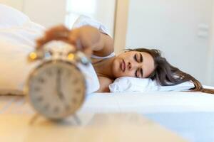 Woman lying in bed turning off an alarm clock in the morning at 5am. Hand turns off the alarm clock waking up at morning, girl turns off the alarm clock waking up in the morning from a call. photo