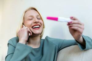 Smiling young woman looking on pregnancy test. Happy woman with pregnancy test. Smiling girl telling good news on mobile. Family, child expectation and maternity concept. Copy space photo