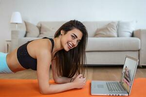 Portrait of young attractive woman doing exercises while watching online lessons on her laptop. Healthy lifestyle and sports concept. Shot of fitness woman sitting on exercise mat photo