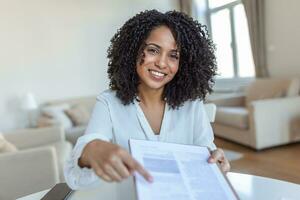 Sign Here. Young smiling confident woman pointing to a contract, sheet of paper, holding a pen, looking and showing it at camera. Presentation, Agreement, Business Concept. photo