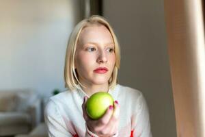 Young beautiful woman eating fresh apple and looking through window. photo