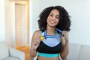 retrato de un atractivo joven hembra atleta posando con su oro medalla. africano americano atleta demostración primero sitio medalla foto