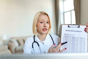 Smiling professional female doctor wearing uniform taking notes in medical journal, filling documents, patient illness history, looking at laptop screen, student watching webinar photo