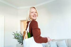 Beautiful young woman with vegetables in grocery bag at home. Portrait of a happy young woman holding a bag full of healthy vegetables at home. Healthy food first photo