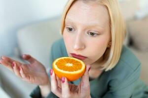 Sick woman trying to sense smell of half fresh orange, has symptoms of Covid-19, corona virus infection - loss of smell and taste. One of the main signs of the disease. photo