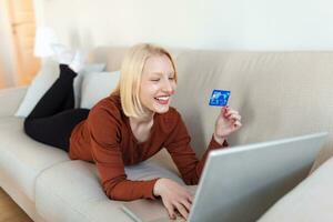 Young Woman On Sofa Shopping Online With Debit Card. Beautiful girl using laptop computer for online shopping at home photo