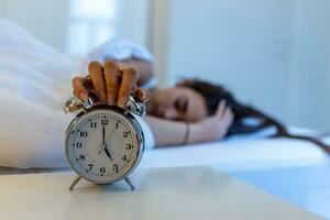 Woman lying in bed turning off an alarm clock in the morning at 5am. Hand turns off the alarm clock waking up at morning, girl turns off the alarm clock waking up in the morning from a call. photo