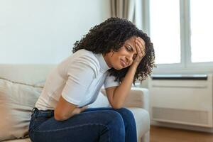 Woman in painful expression holding hands against belly suffering menstrual period pain, lying sad on home bed, having tummy cramp in female health concept photo