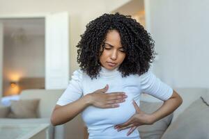 Young African American woman palpating her breast by herself that she concern about breast cancer. Healthcare and breast cancer concept photo