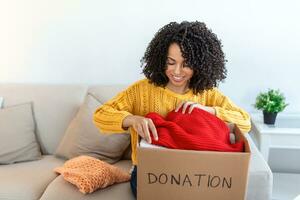 Donation Concept. Woman holding a Donate Box with full of Clothes. Woman holding a book and clothes donate box. Clothes in box for concept donation and reuse recycle photo