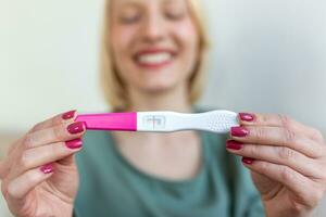 el embarazo, Fertilidad, maternidad y personas concepto - contento sonriente mujer mirando a el embarazo prueba a hogar foto