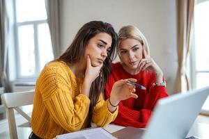 Clever female students discussing ideas for coursework project reading information from network on laptop computer,young women watching tutorial together having conversation in office photo