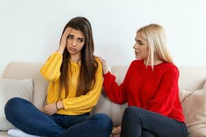 Friend trying to calm down her friend. Woman crying. Young lady sharing her problem with friend. female in depression. Woman comforting hes sad friend sitting on a couch in the living room at home photo