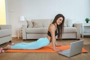 Young woman exercising at home in a living room. Video lesson. Young woman repeating exercises while watching online workout session. Beautiful young woman doing fitness exercise at home photo