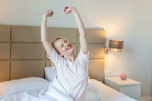 Woman stretching in bed with her arms raised. Portrait of attractive lovely girl enjoying time in bad after sleeping lying under blanket making stretching keeping eyes closed. Good day life health photo