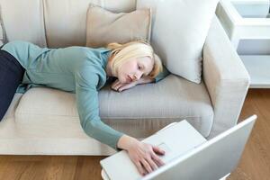 Exhausted young woman lying on sofa, using laptop, too tired or bored of online work at home, free space. Workaholism, chronic fatigue, overworking on remote job concept photo