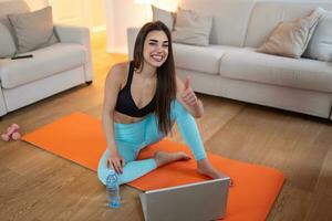 Woman training at home, doing workout and watching videos on laptop. Beautiful woman is doing exercise. She is watching video on the internet and repeating the tasks photo