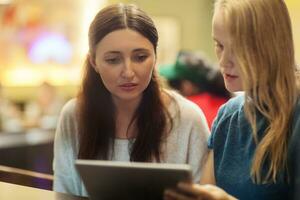 Two women have a discussion in the restaurant using electronic tablet photo