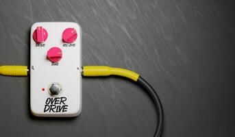 White Guitar Pedal, Overdrive, Viewed From Above, Pink Kinobs Connected To Two Cables On The Floor, On Black Background photo