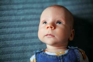 un pequeño chico, recién nacido, con hermosa azul ojos mira dentro el distancia foto