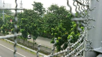 View of trees from broken iron wire fence over highway photo