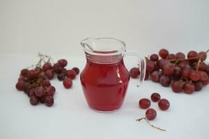 uva jugo en un vaso jarra con Fresco uvas en un blanco antecedentes foto