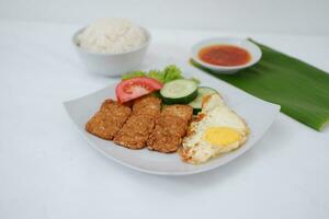 Fried tempeh cutlet with rice and fried egg on white plate photo