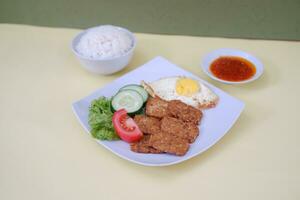 Fried tempeh cutlet with rice and fried egg on white plate photo