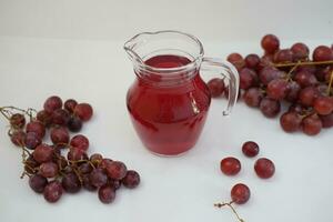 uva jugo en un vaso jarra con Fresco uvas en un blanco antecedentes foto