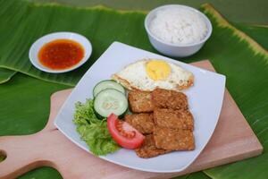 Fried tempeh cutlet with rice and fried egg on white plate photo