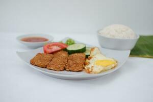 Fried tempeh cutlet with rice and fried egg on white plate photo