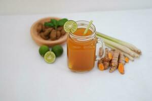 Fresh ginger and lemon juice in a glass jar with ginger roots on white background. photo