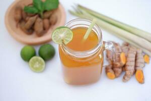 Fresco jengibre y limón jugo en un vaso tarro con jengibre raíces en blanco antecedentes. foto