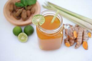 Fresco jengibre y limón jugo en un vaso tarro con jengibre raíces en blanco antecedentes. foto