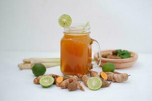 Fresco jengibre y limón jugo en un vaso tarro con jengibre raíces en blanco antecedentes. foto