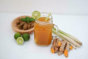 Fresh ginger and lemon juice in a glass jar with ginger roots on white background. photo