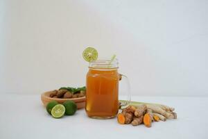 Fresco jengibre y limón jugo en un vaso tarro con jengibre raíces en blanco antecedentes. foto