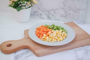 congelado vegetales en un blanco plato en un blanco mármol mesa. foto