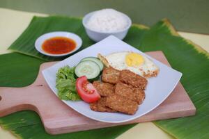 Fried tempeh cutlet with rice and fried egg on white plate photo