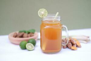 Fresh ginger and lemon juice in a glass jar with ginger roots on white background. photo