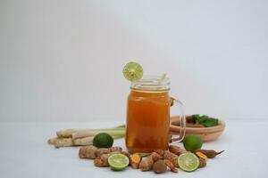 Fresco jengibre y limón jugo en un vaso tarro con jengibre raíces en blanco antecedentes. foto