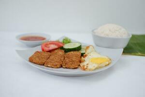 Fried tempeh cutlet with rice and fried egg on white plate photo