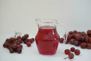 uva jugo en un vaso jarra con Fresco uvas en un blanco antecedentes foto